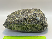 A smooth, shiney or scaly mostly green piece of serpentinite, tapered on both ends like a watermelon seed.